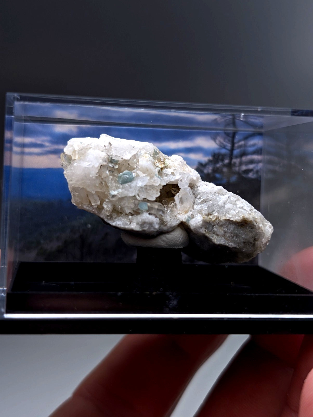 A white crystalline quartz specimen with blue-green cookeite and yellow inclusions in a clear acrylic case