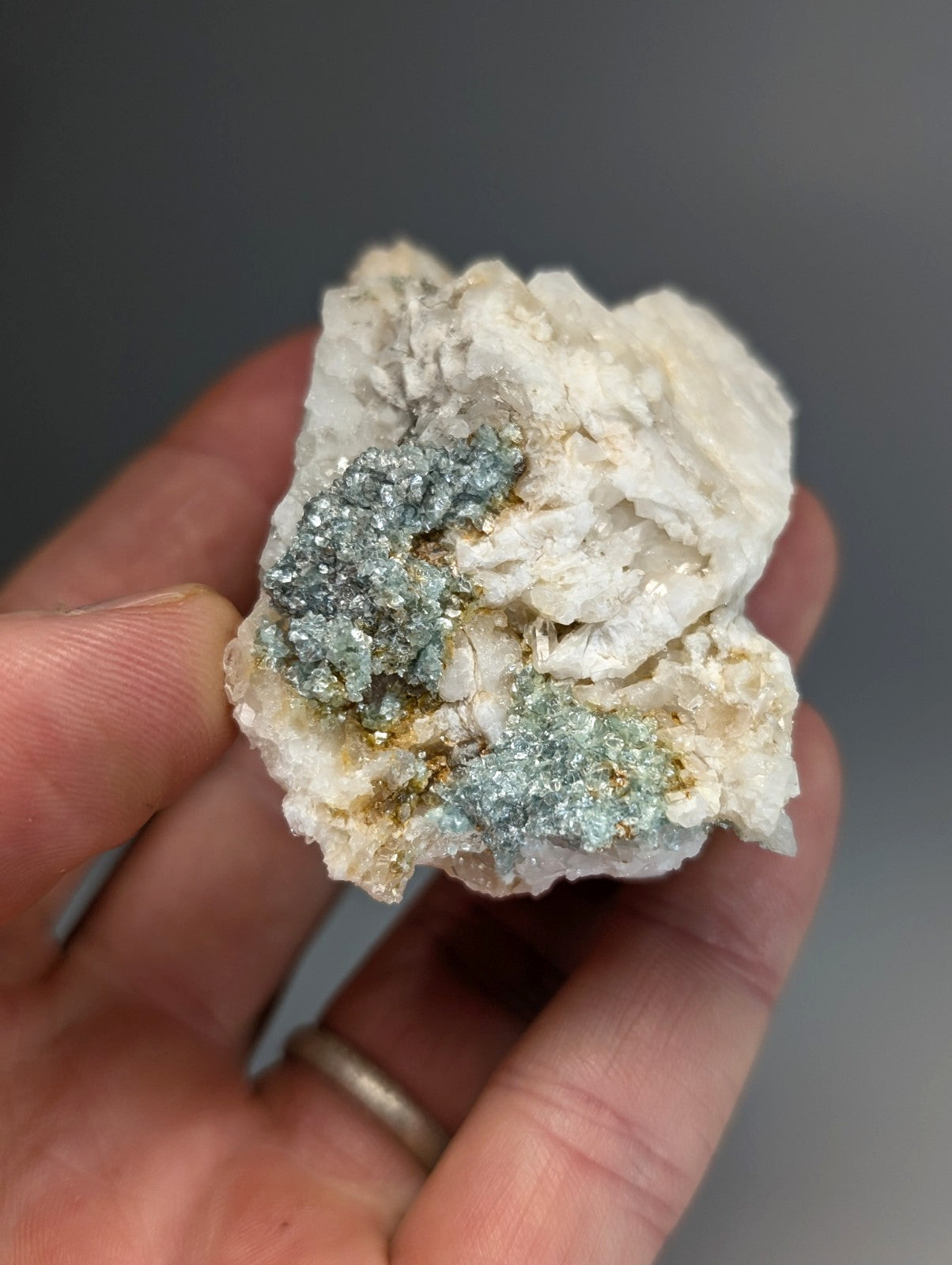 A hand holds blue green cookeite on white quartz with shimmering metallic mineral growths from saline county Arkansas