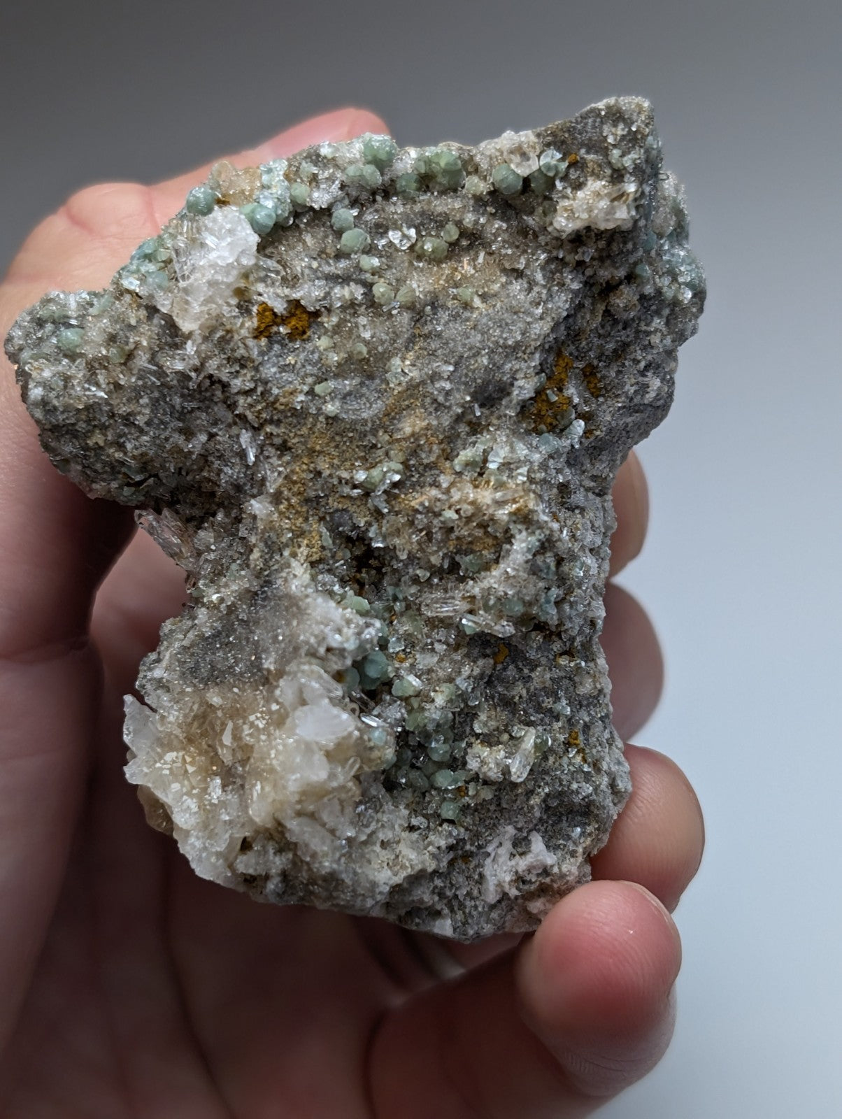 A hand holds a rare blue green cookeite on quartz specimen with translucent and greenish blue crystals from Arkansas