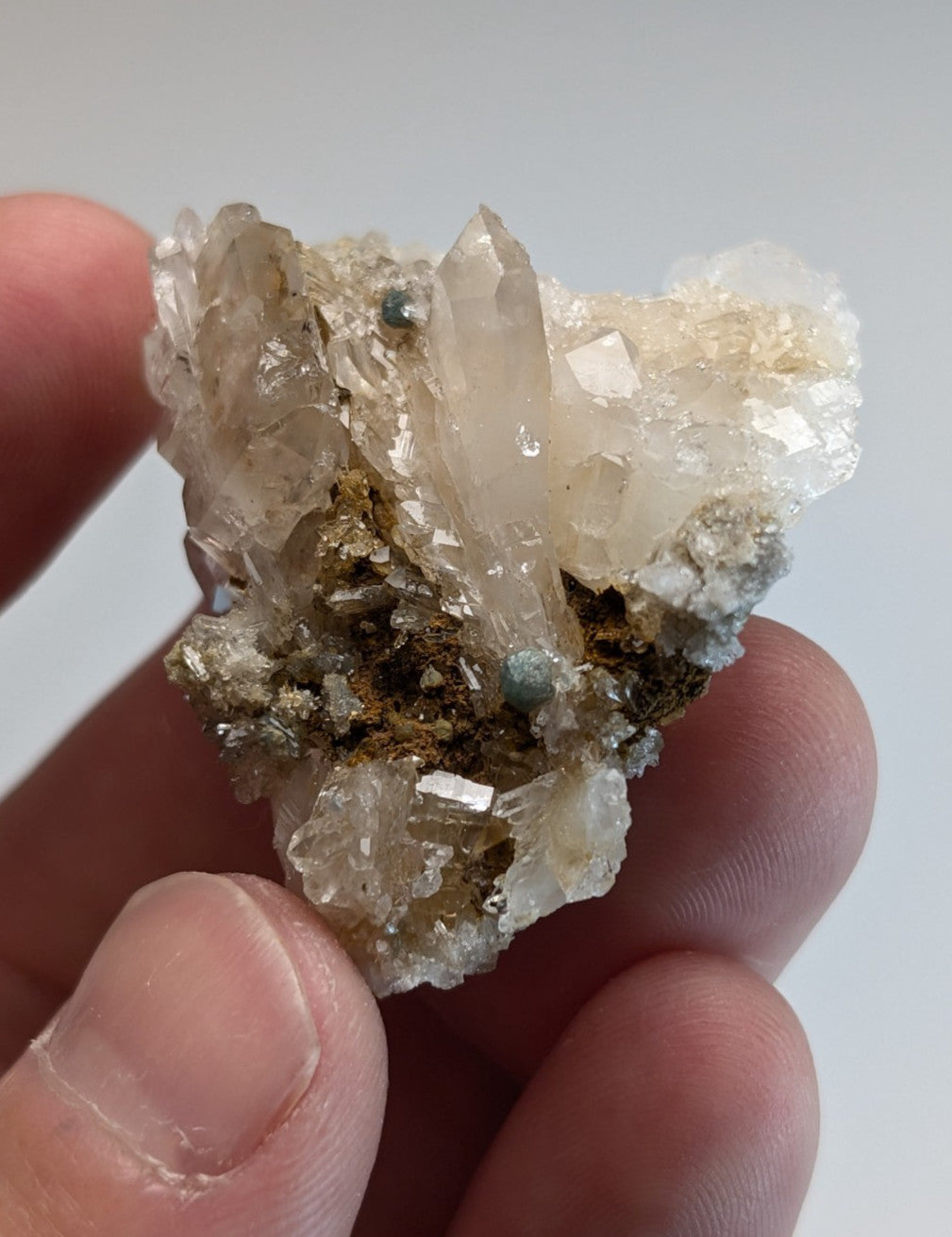 A translucent quartz crystal cluster with blue green cookeite and metallic mineral inclusions held between fingers