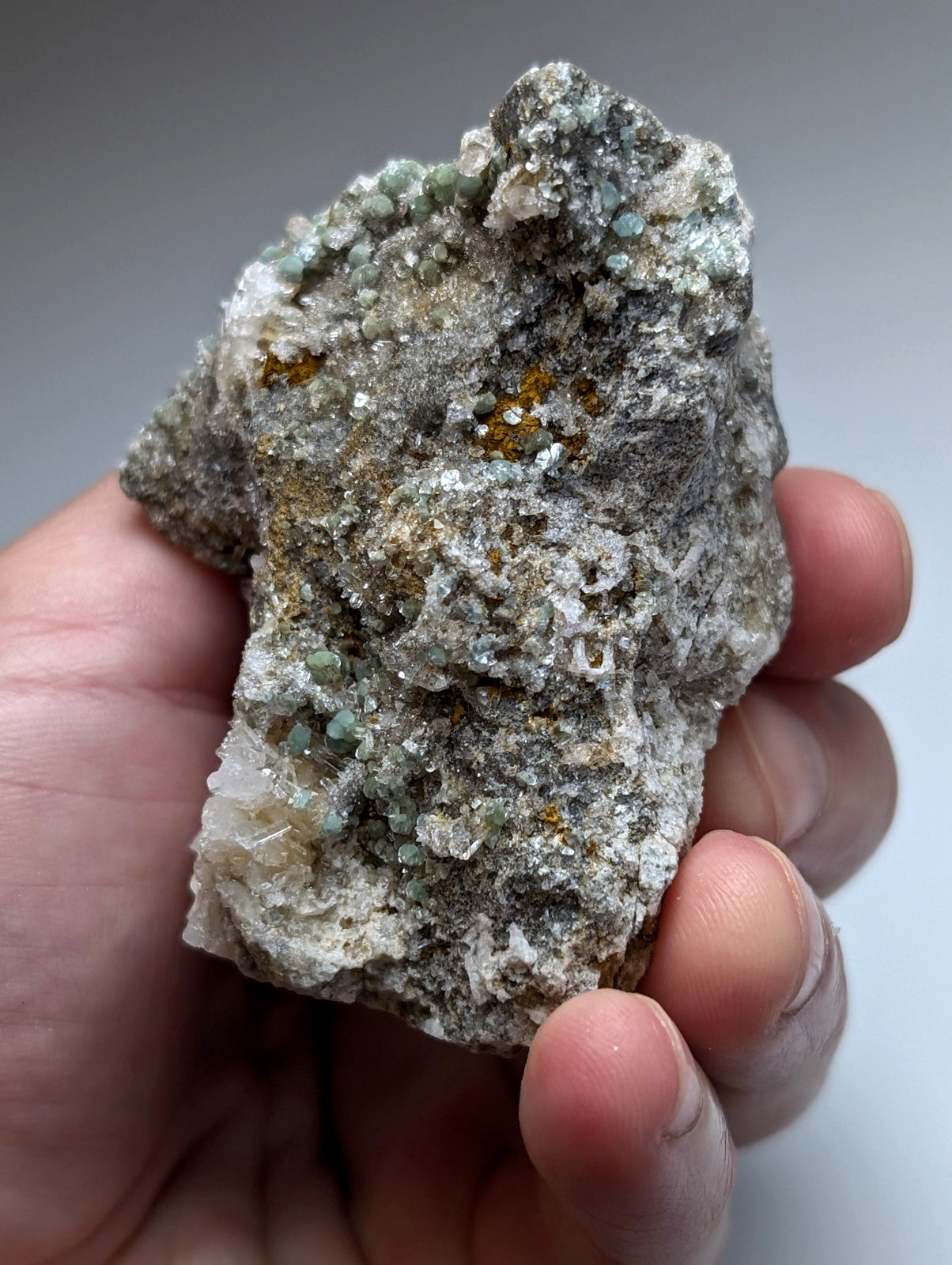 A hand holds blue green cookeite on quartz with green crystals and orange yellow specks from saline county Arkansas