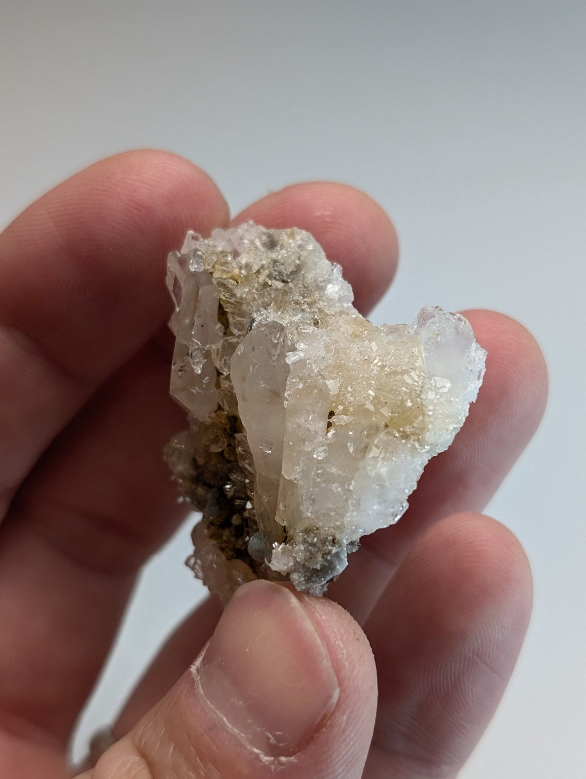 A translucent white quartz cluster with golden inclusions held between fingers blue green cookeite rare uv reactive