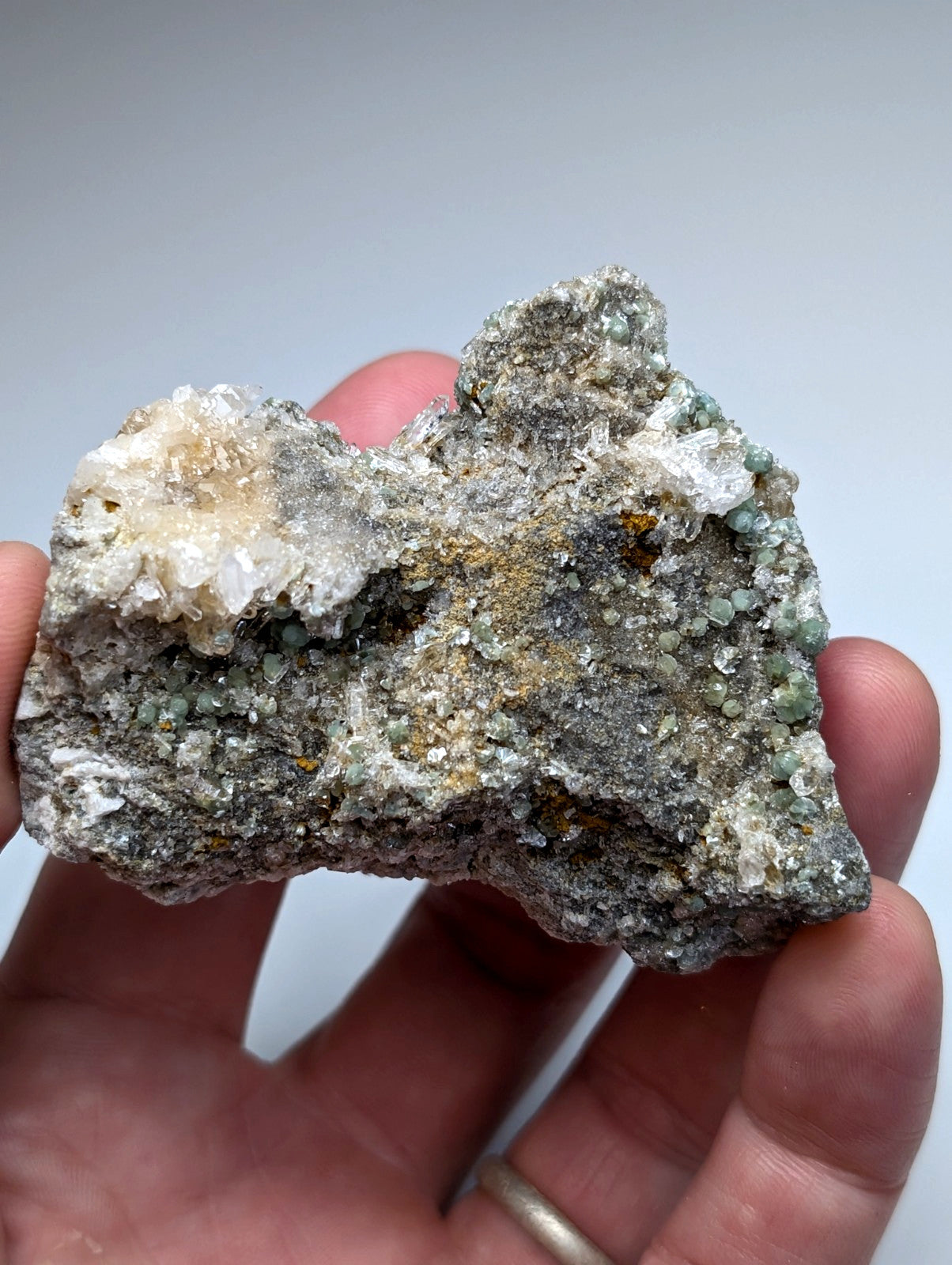 A hand holds a rare blue green cookeite on quartz mineral with translucent white crystals and greenish blue speckles