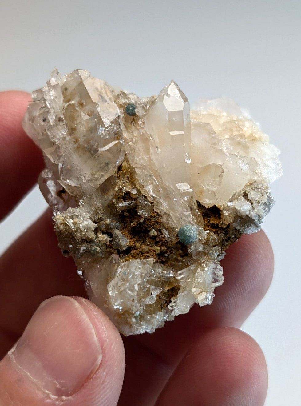 A translucent quartz crystal cluster with blue green cookeite and turquoise specks held in hand from Arkansas