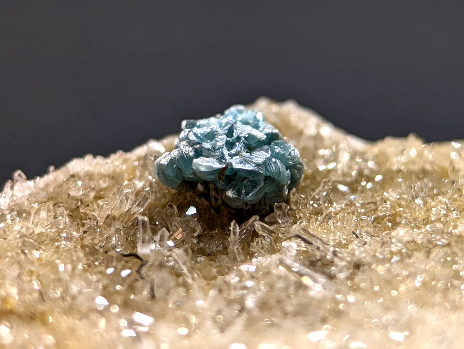 A vibrant turquoise-blue mineral specimen with a rough, clustered texture sits atop a bed of translucent golden-yellow crystals.