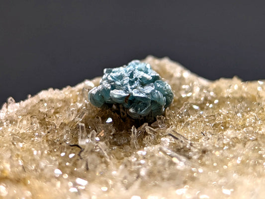 A vibrant turquoise-blue mineral specimen with a rough, clustered texture sits atop a bed of translucent golden-yellow crystals.