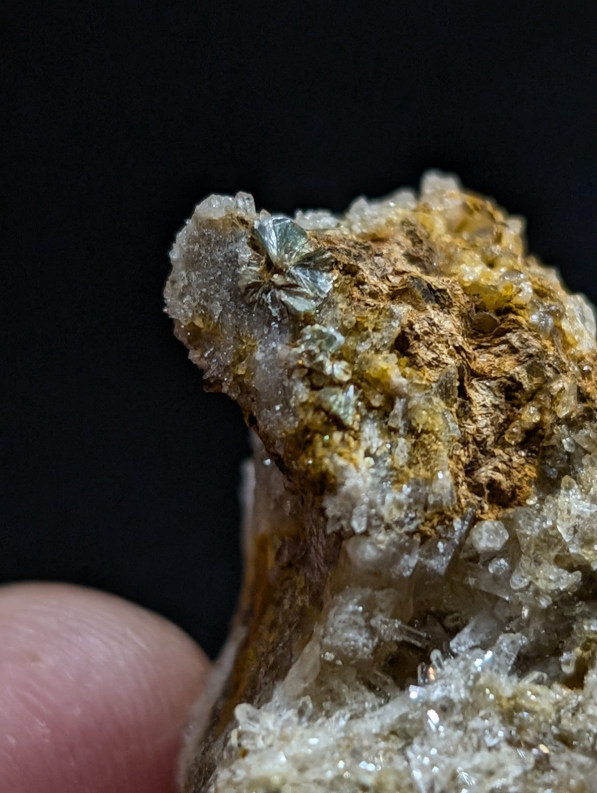 A textured mineral specimen featuring translucent white crystals, golden-brown matrix material, and small metallic greenish-blue crystalline formations.