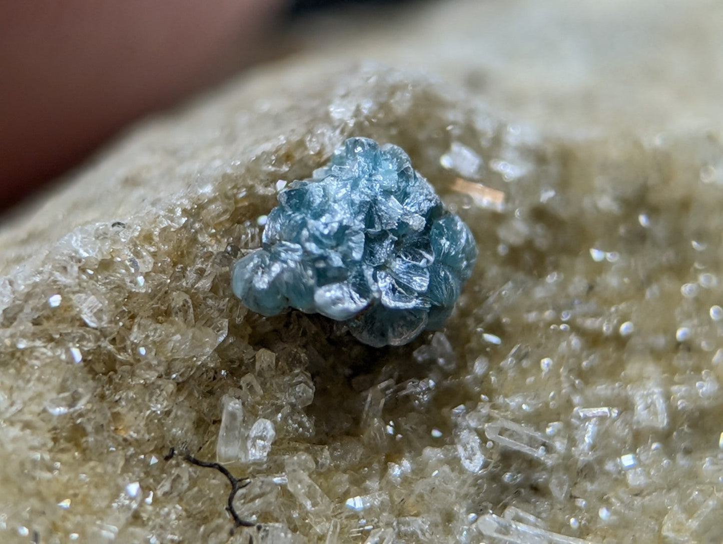A vibrant blue, crystalline gemstone with a rough, clustered texture rests atop a bed of translucent quartz crystals.