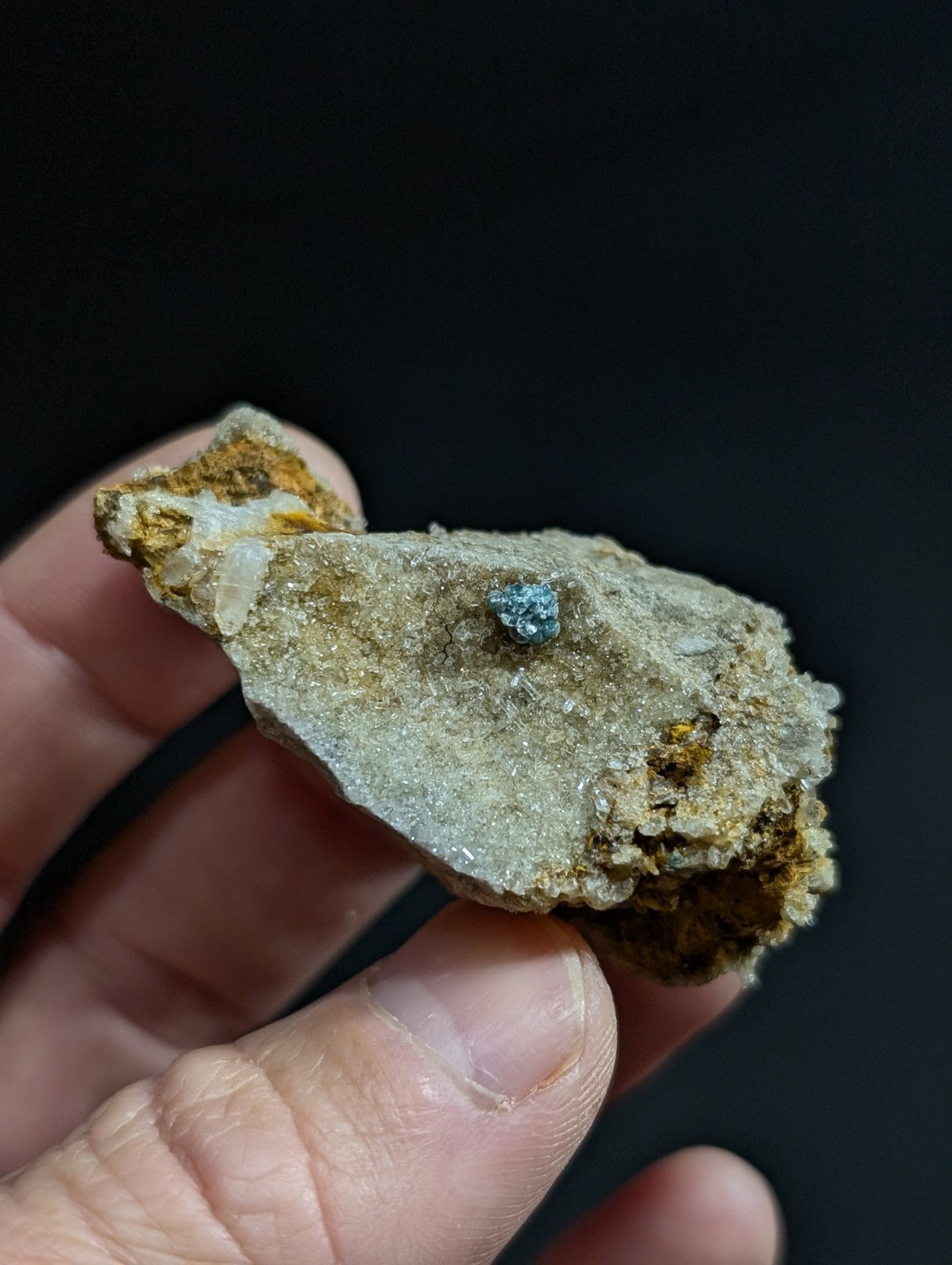 A small, rough-textured mineral specimen with a prominent blue gemstone embedded in its surface.