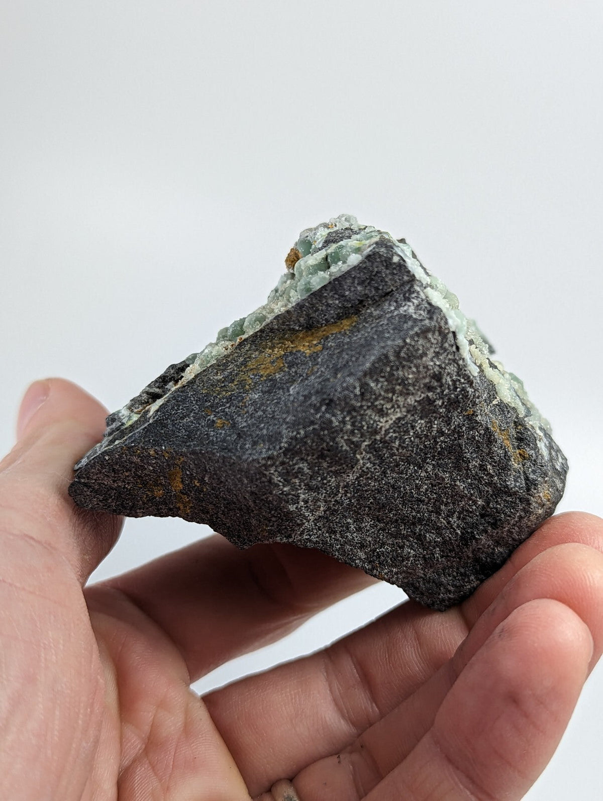 A dark gray rock with patches of light green and yellow mineral deposits.