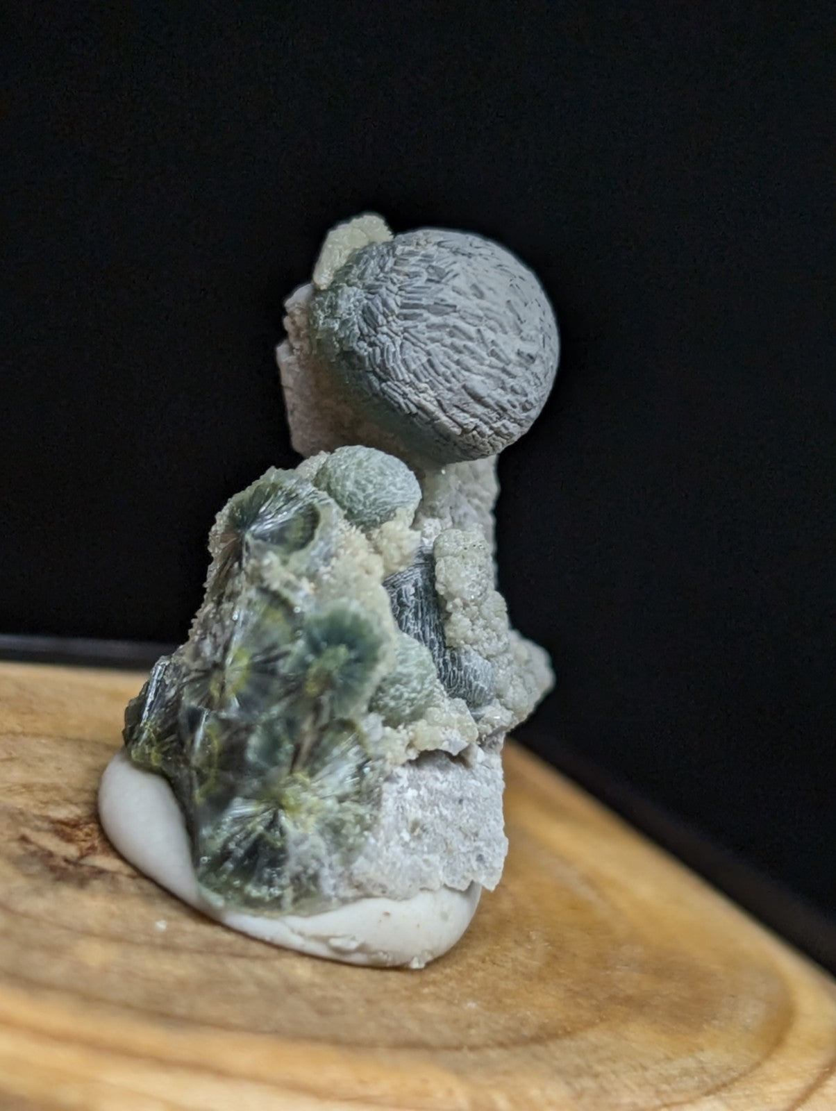 Gray and green mineral specimen with a textured, spherical top resting on a rougher base.