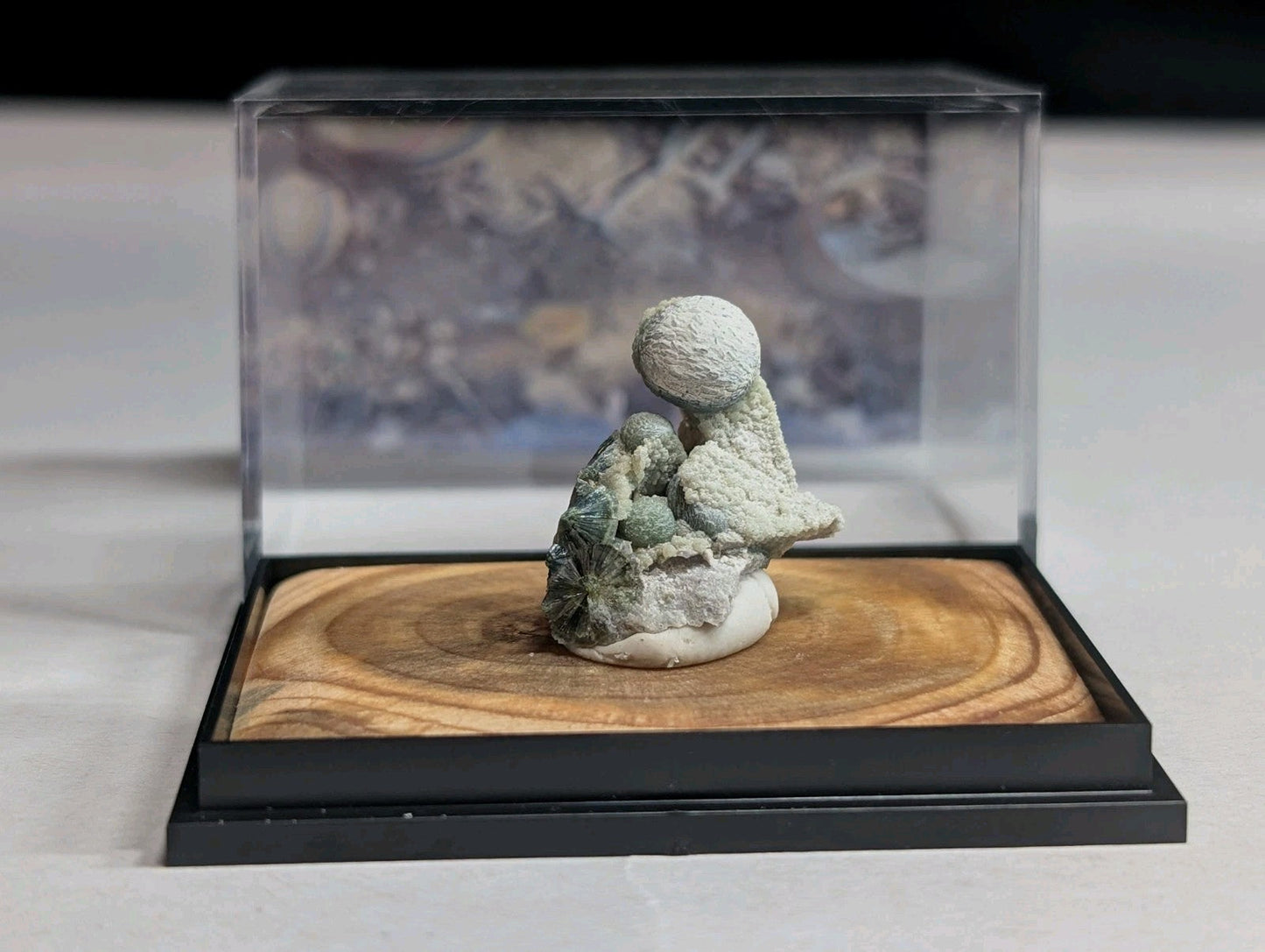 A delicate, pale green and white mineral sculpture of a seated figure nestled within its natural rock formation.