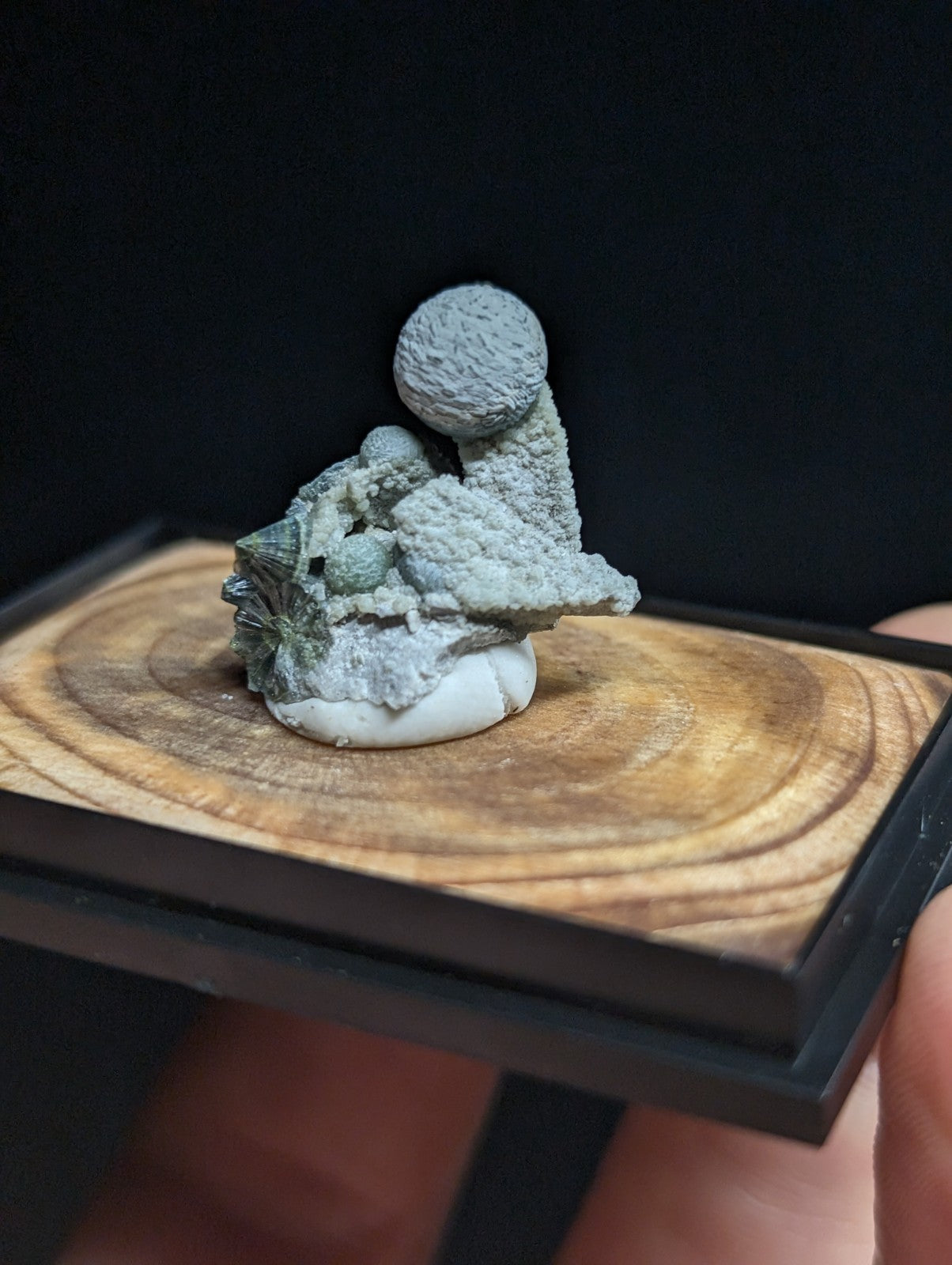 Gray, textured mineral specimen with a spherical top and rocky base, displayed on a wooden platform.