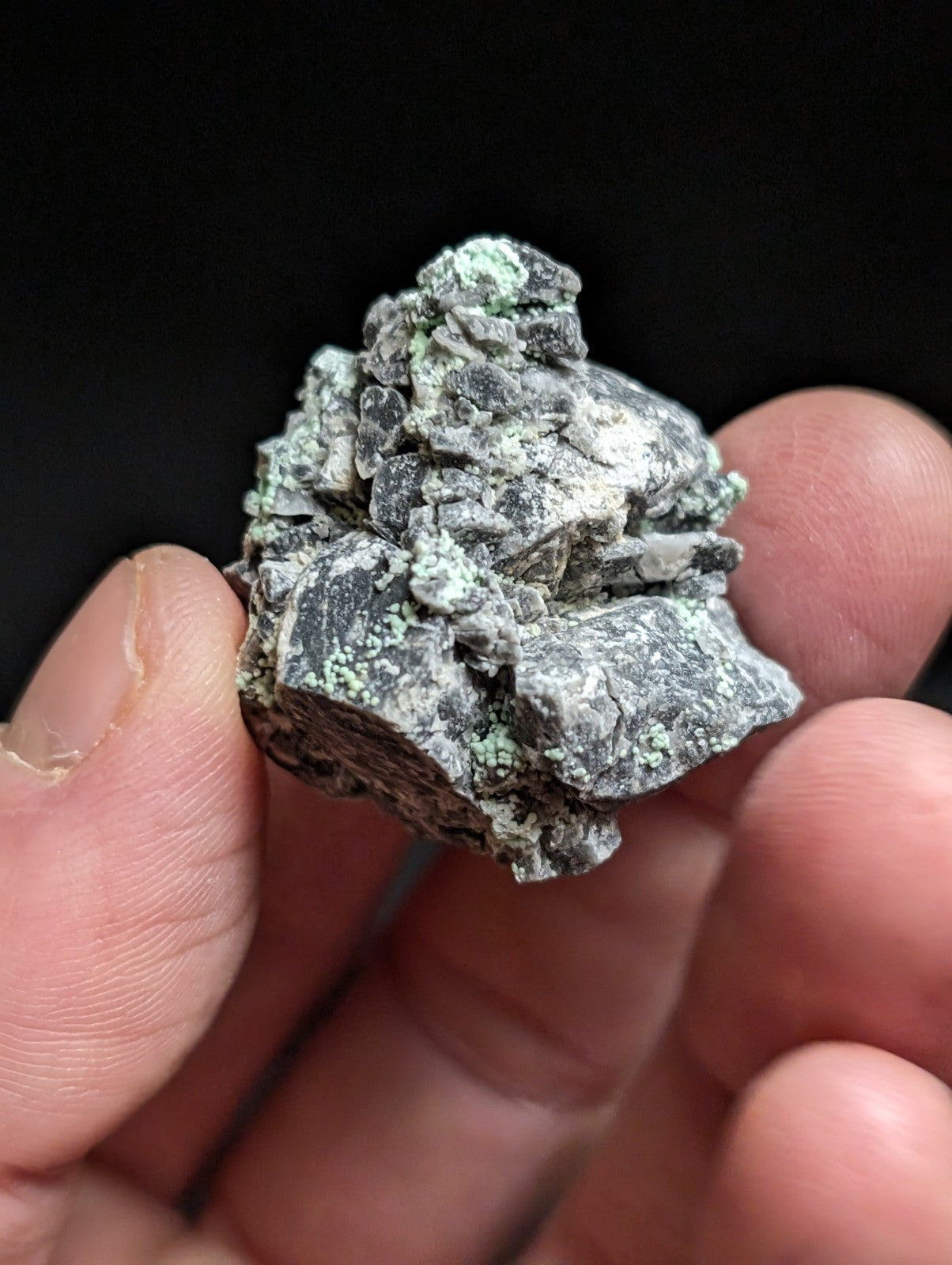 A rough, irregularly shaped mineral specimen with a mottled gray and green surface, featuring patches of verdigris-like patina.