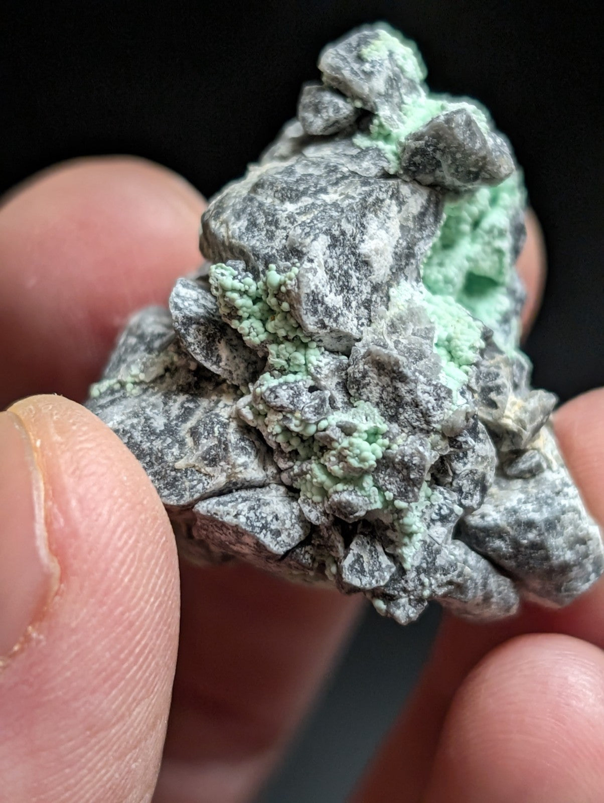 A textured, irregularly shaped mineral specimen with a gray base and patches of vibrant green crystalline growths.