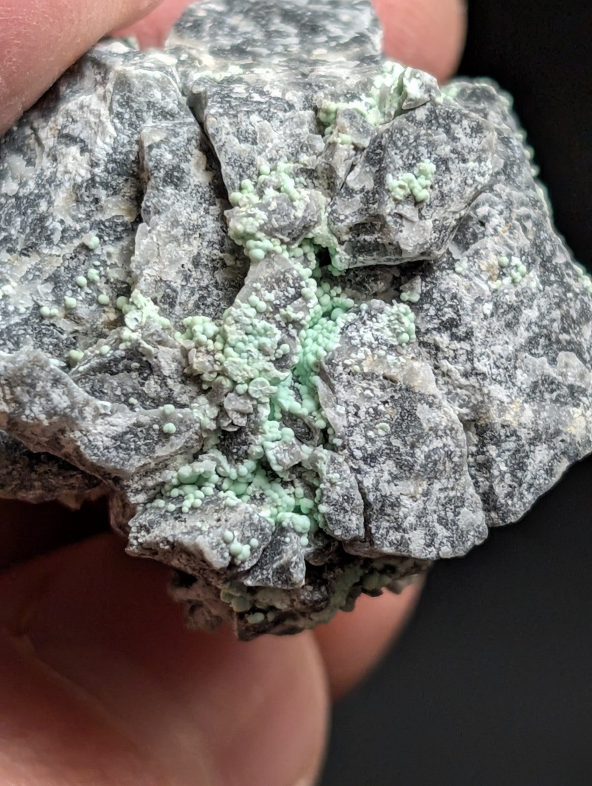 A rough, gray rock specimen featuring vibrant light green crystalline formations.