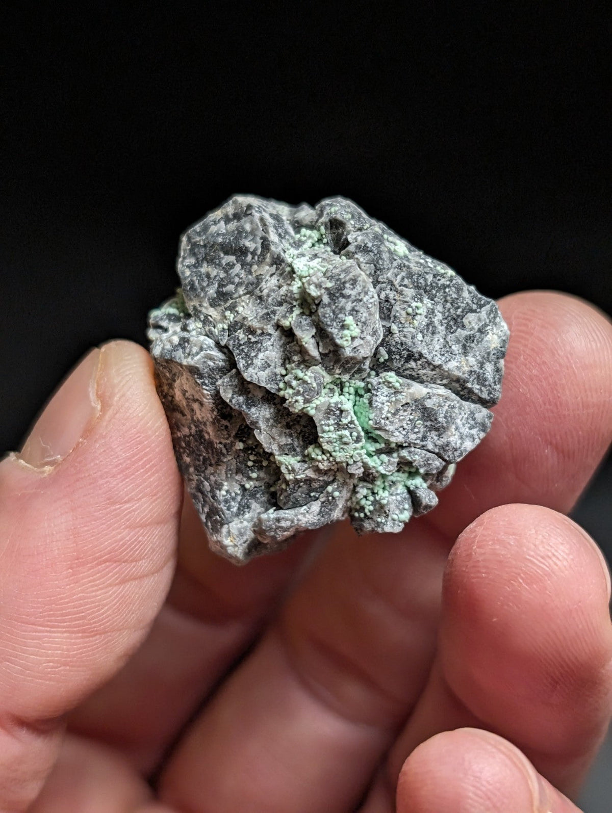 A rough, irregularly shaped mineral specimen with a grayish base and patches of vibrant green crystalline growths.