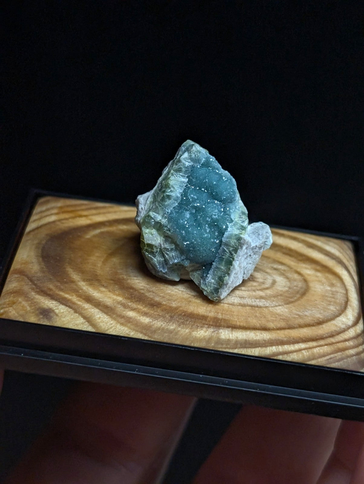 A textured, teal-green mineral specimen with a crystalline surface rests on a wooden display base.