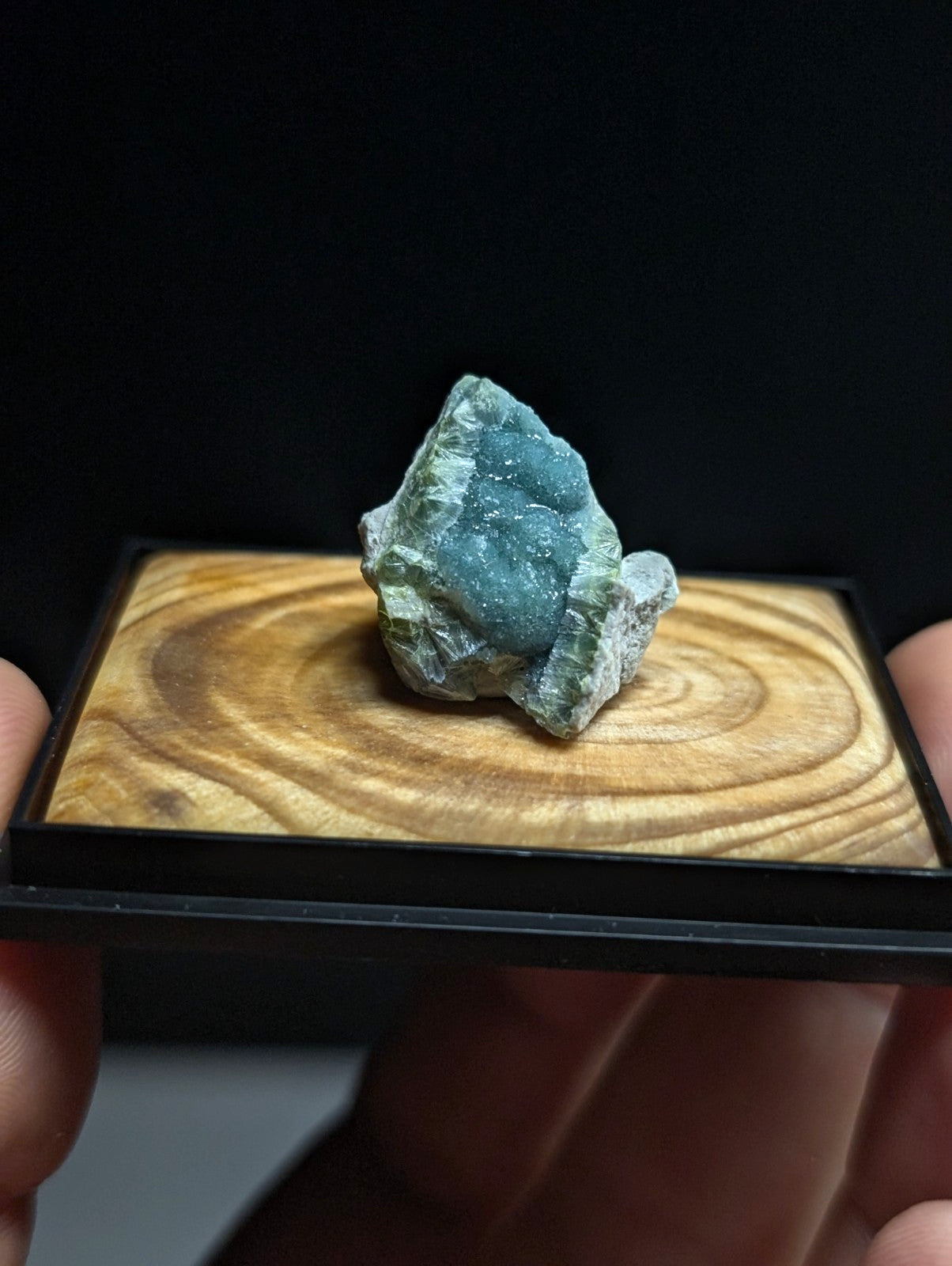 A striking teal-blue mineral specimen with a crystalline, glittering surface and rough, earthy greenish-gray base.
