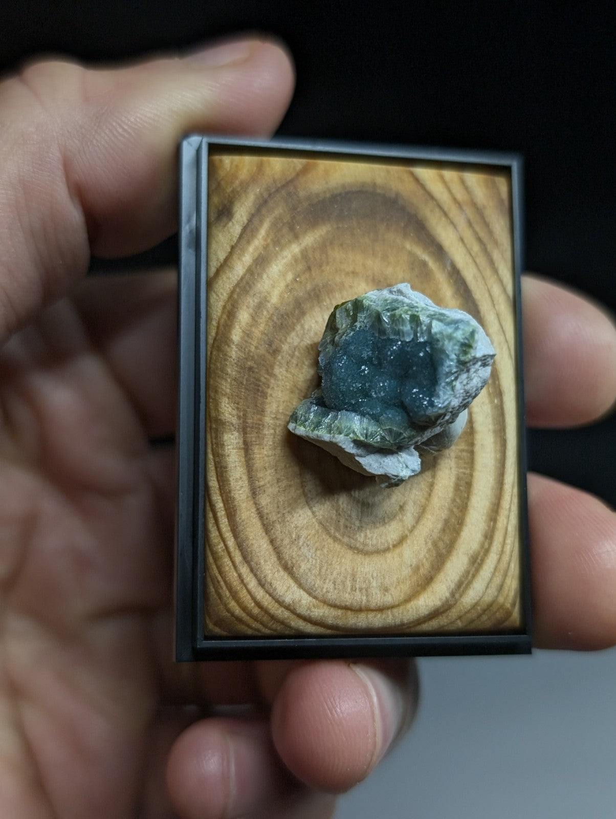 A natural green and blue mineral specimen with a rough, crystalline surface is displayed in a small black-framed wooden showcase.