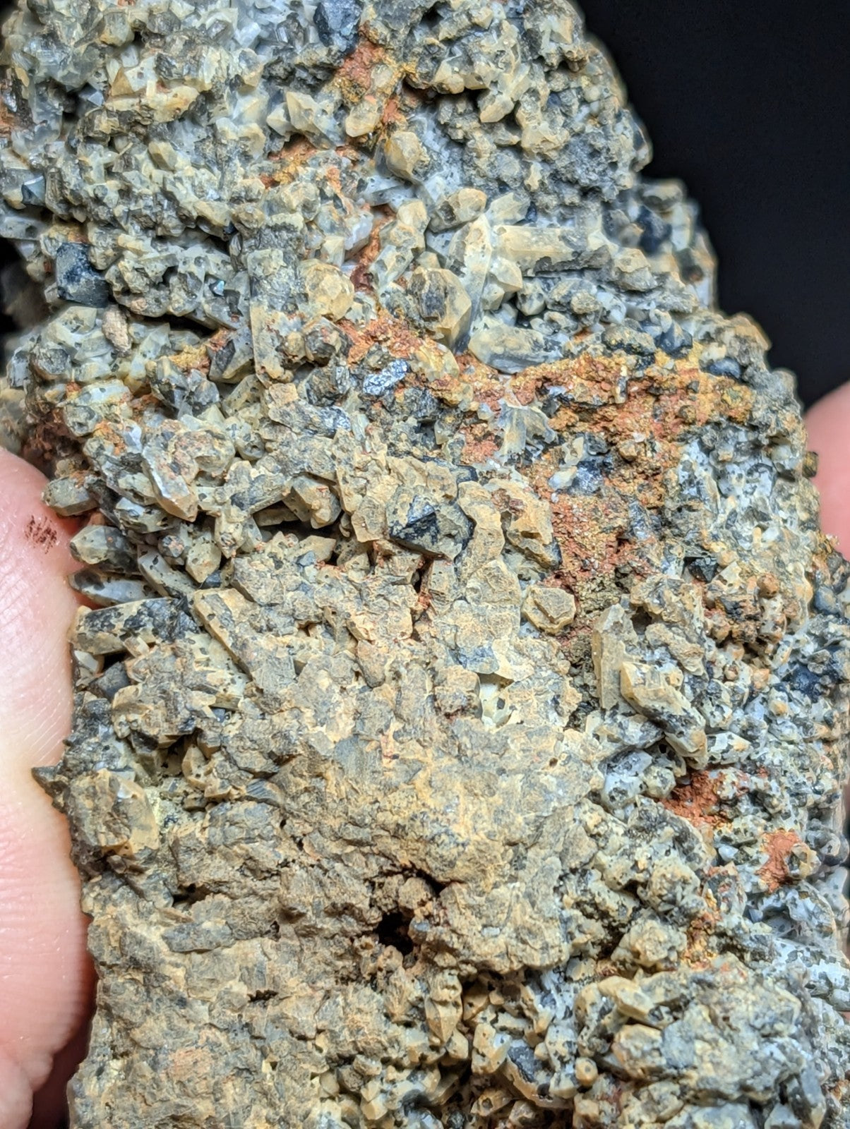 A rugged, textured mineral specimen with a mix of grayish-green crystals and patches of reddish-orange oxidation.
