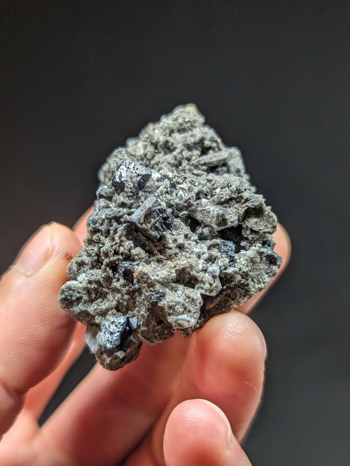 A rough, irregularly shaped mineral specimen with a grayish-green hue and visible crystalline structures.