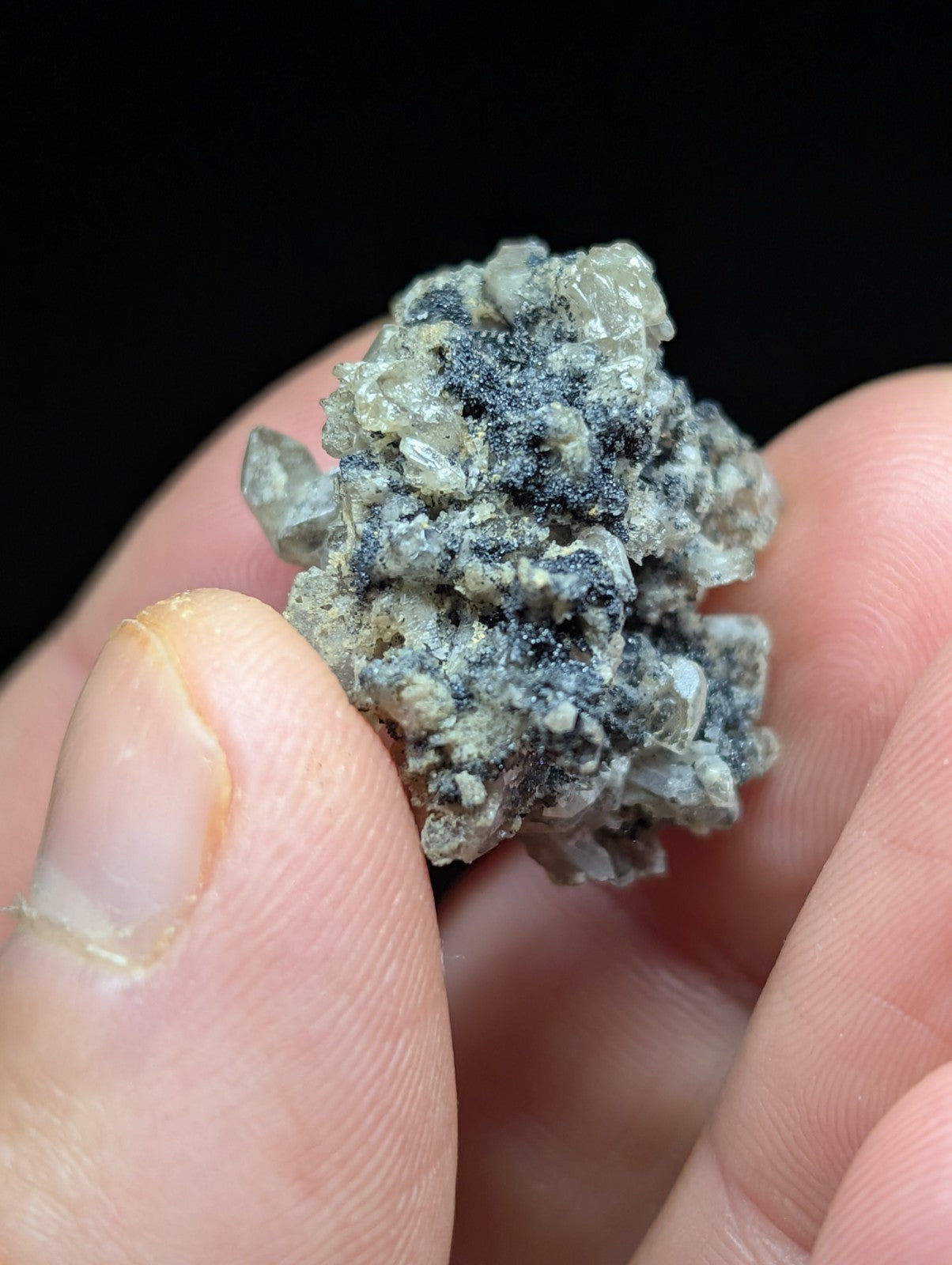 A textured, grayish mineral specimen with translucent crystalline formations and dark speckles.