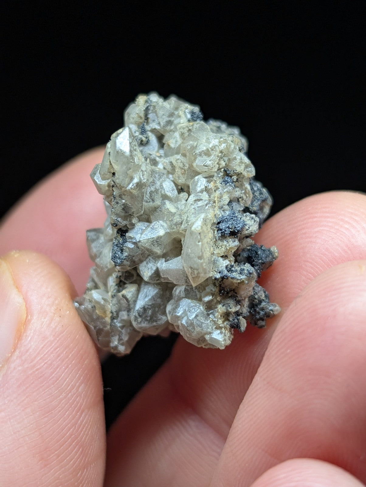 A cluster of translucent, grayish-white crystals with dark mineral inclusions.