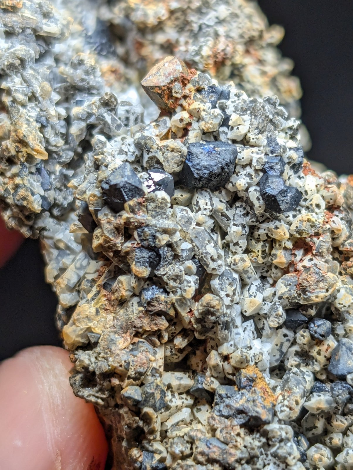 A cluster of dark, faceted mineral crystals embedded in a matrix of gray and yellowish rock.
