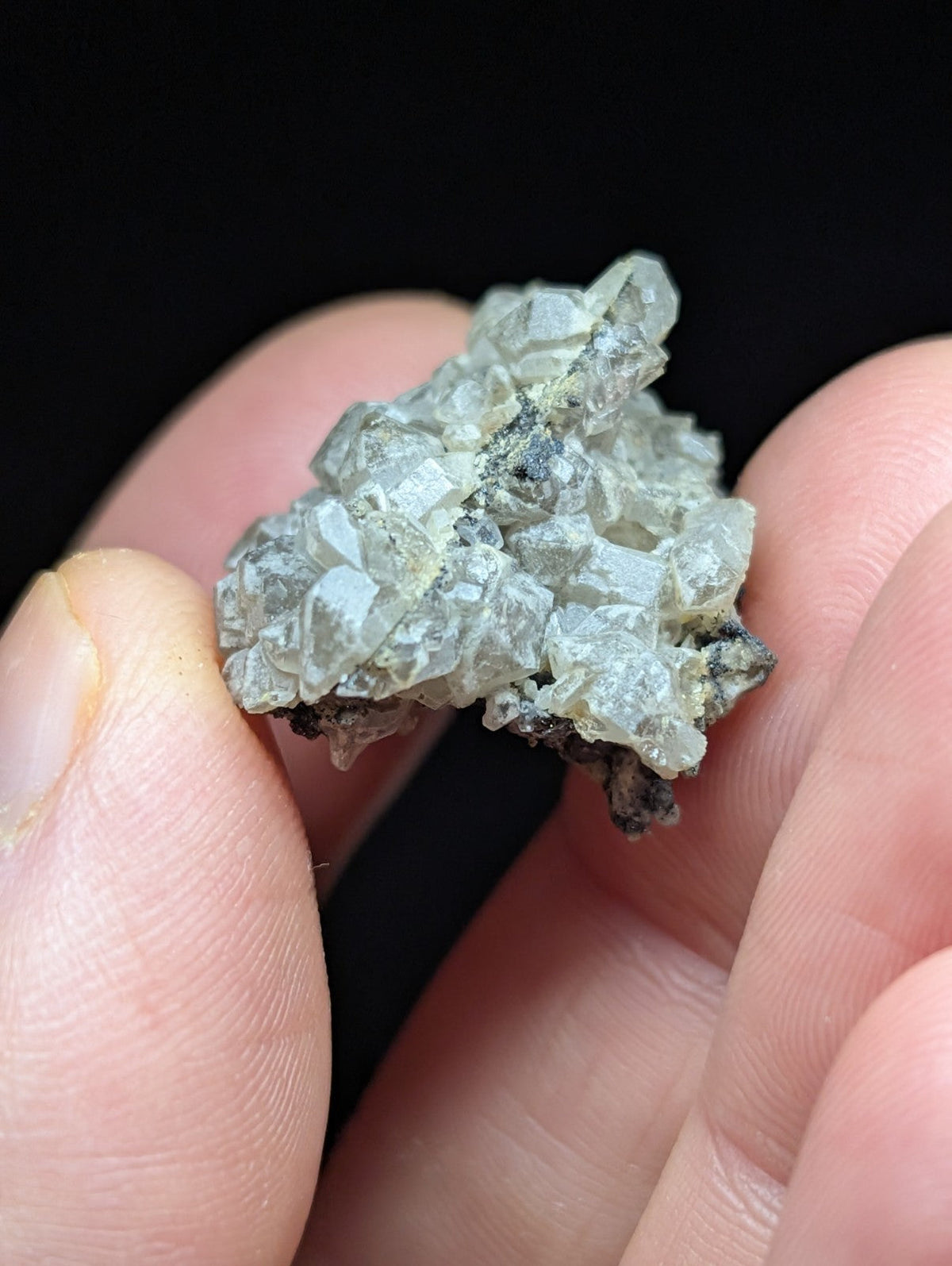 A cluster of translucent, pale gray crystals with sharp facets and some darker mineral inclusions.