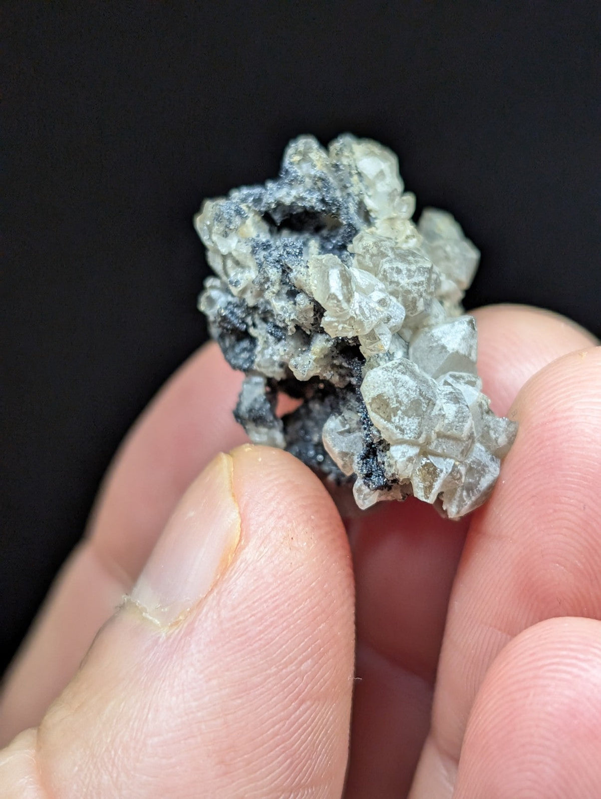 A textured, grayish-white mineral specimen with crystalline formations and dark speckles.