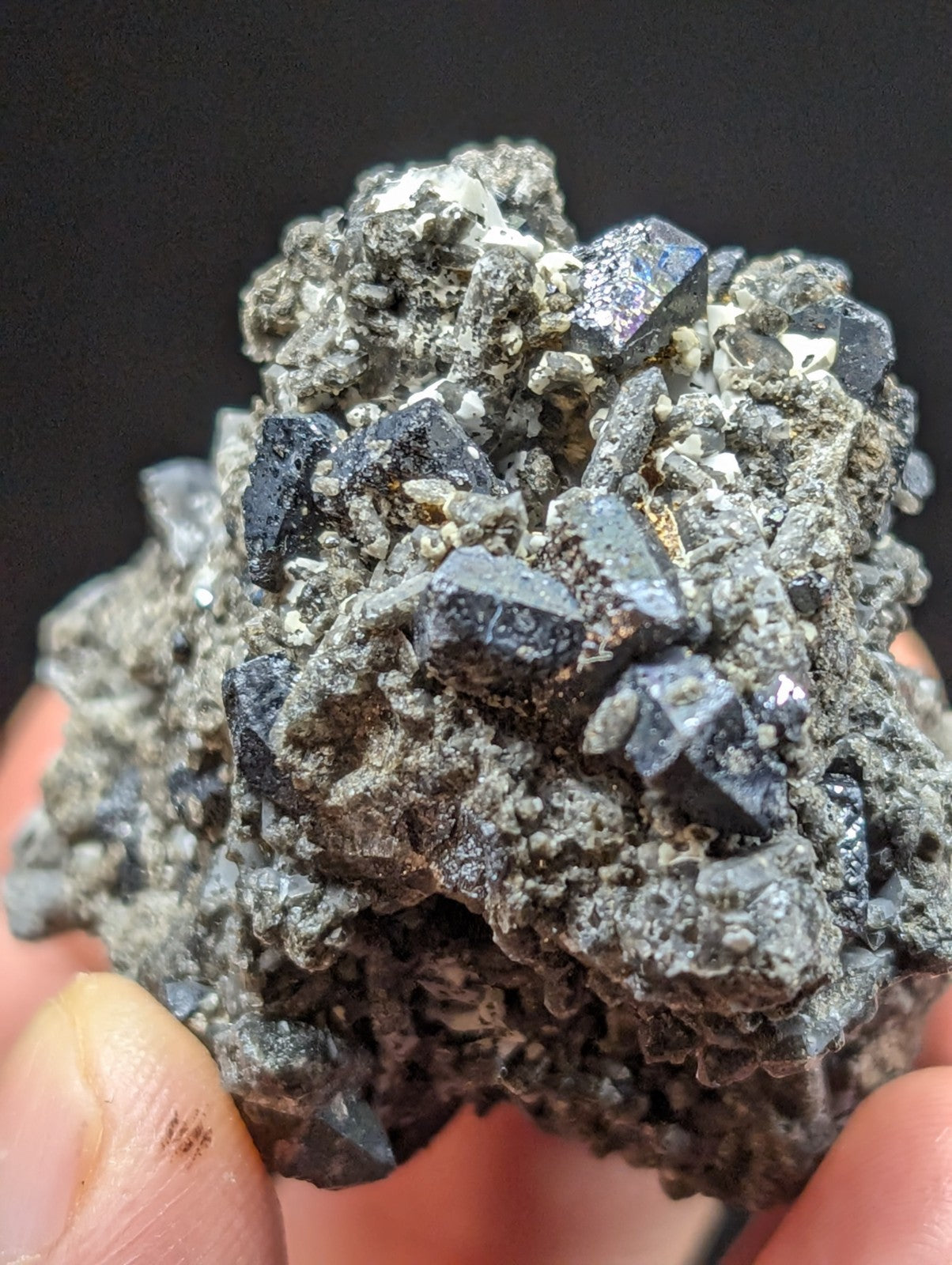 A cluster of dark, metallic-looking pyrite crystals embedded in a rough gray matrix.