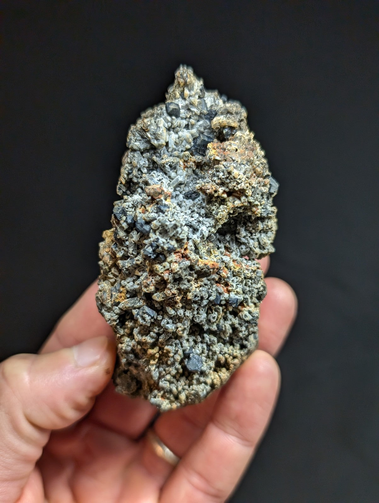 A rough, irregularly shaped mineral specimen with a textured surface featuring patches of gray, black, and subtle orange hues.
