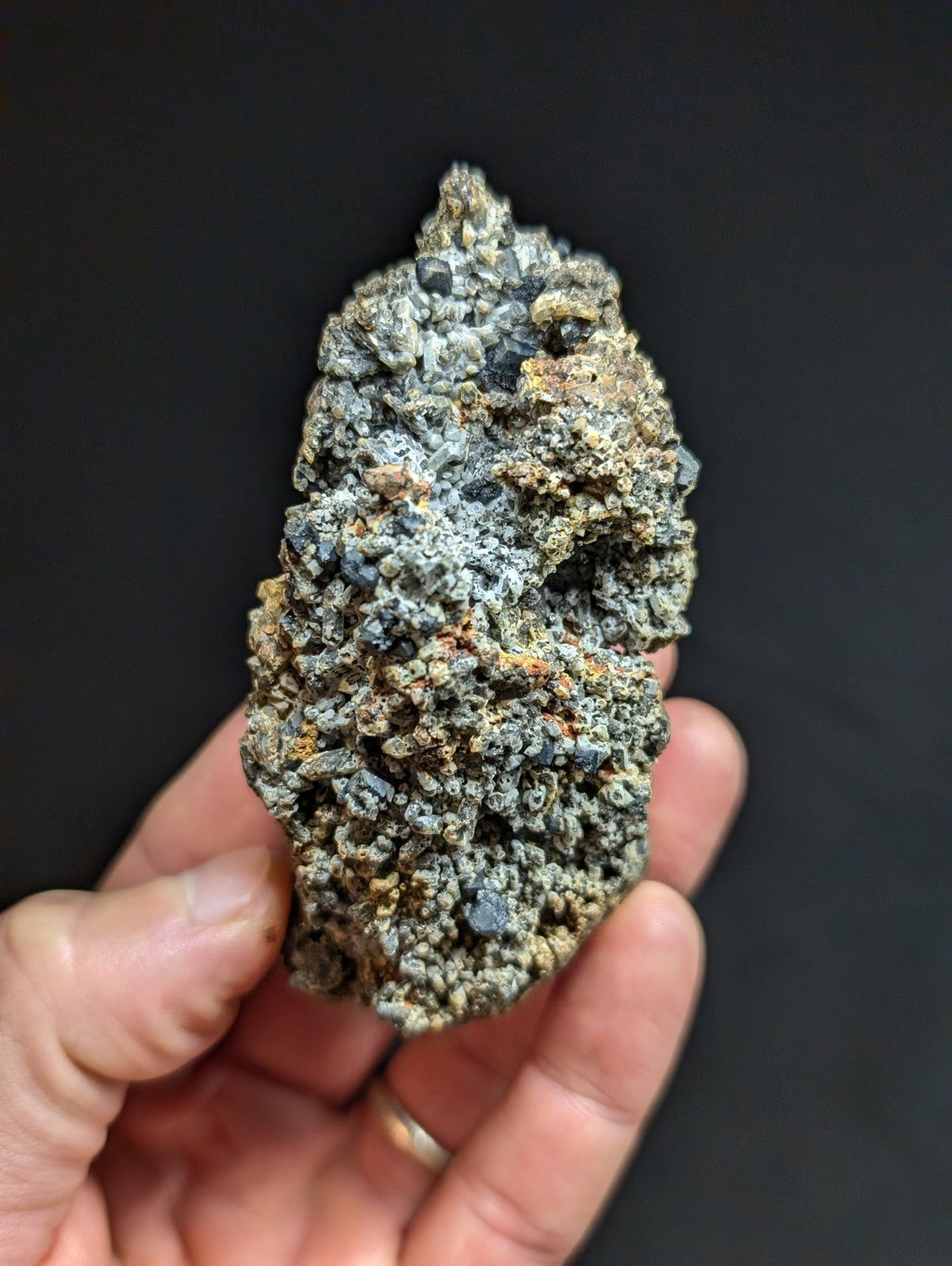 A rough, irregularly shaped mineral specimen with a textured surface featuring patches of gray, black, and subtle orange hues.