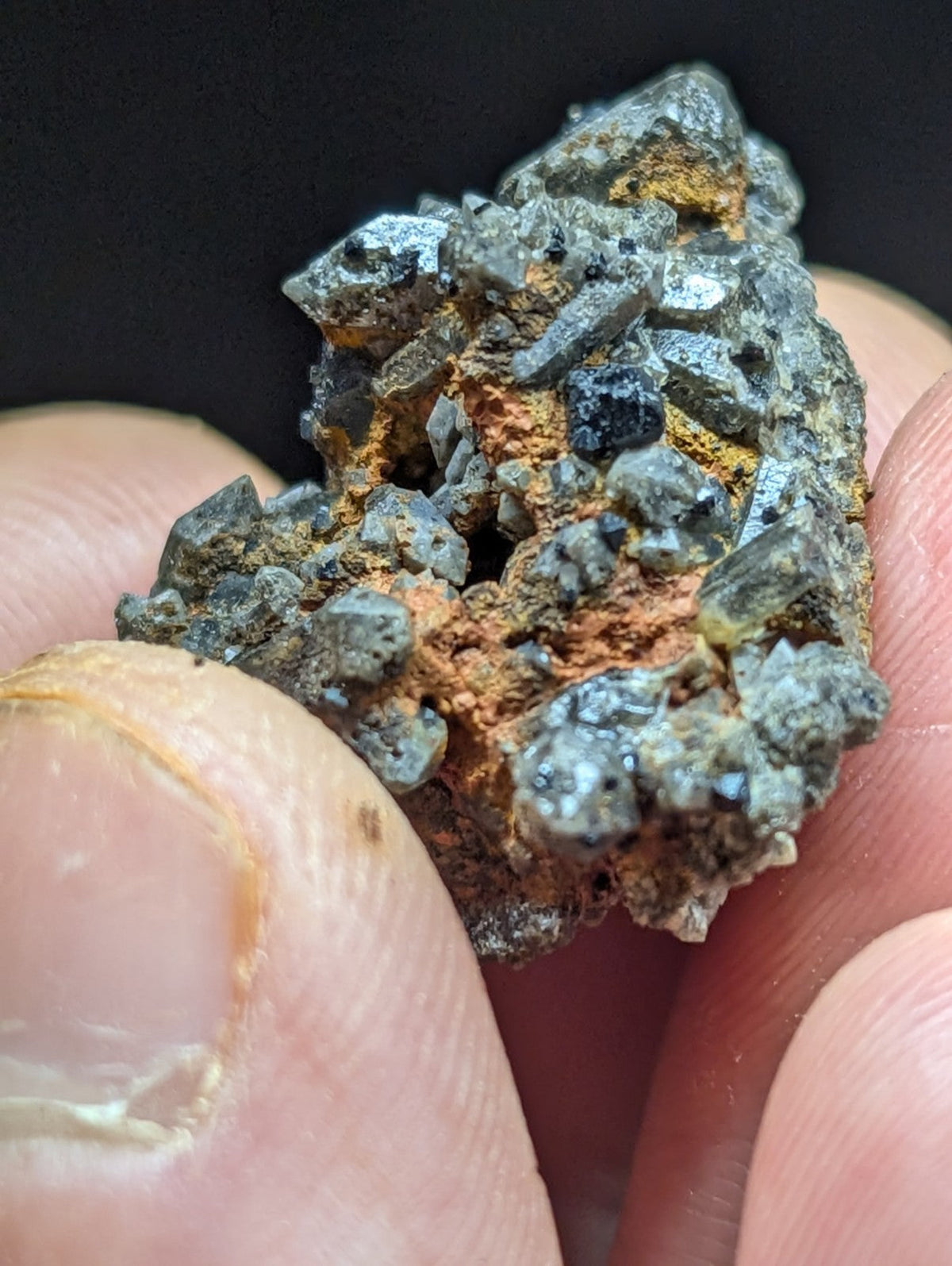 A rugged, irregularly shaped mineral specimen featuring a mix of dark gray and black crystalline formations interspersed with patches of orange-red rust-colored material.