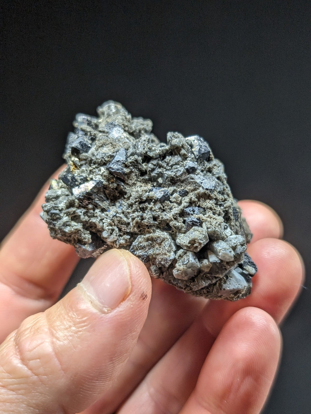 A rough, grayish mineral specimen with a clustered, crystalline texture and small dark inclusions.