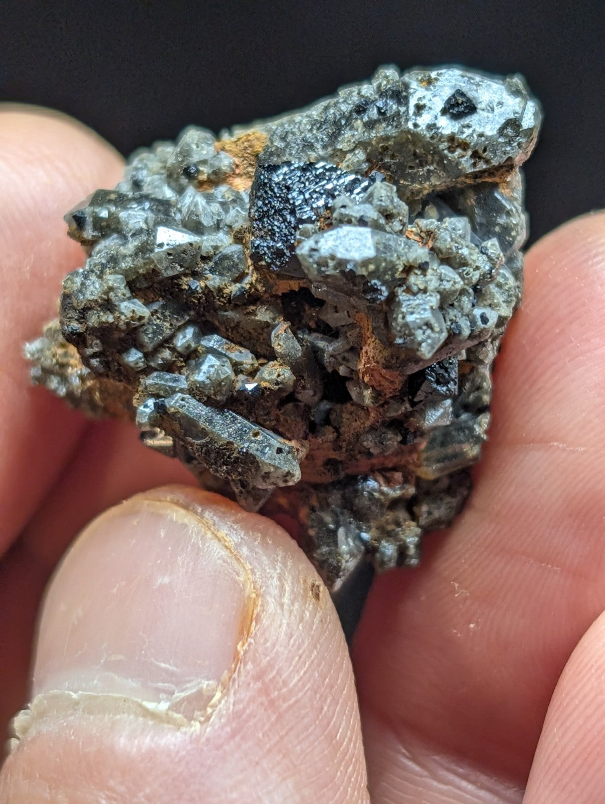 A rugged, grayish-black mineral specimen with a rough, crystalline texture and scattered patches of orange rust.