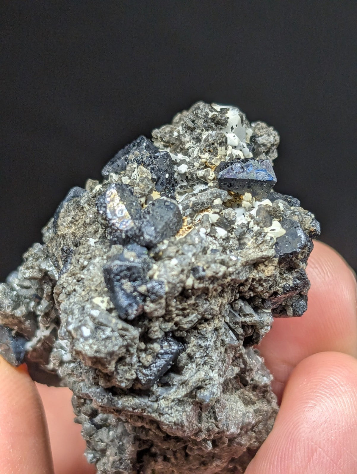 A rugged, dark gray mineral specimen with prominent deep blue crystalline formations embedded in a rough-textured matrix.