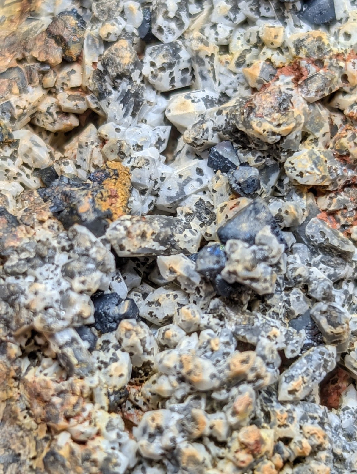 A cluster of speckled, crystalline minerals with a mix of white, gray, black, and orange-brown hues.