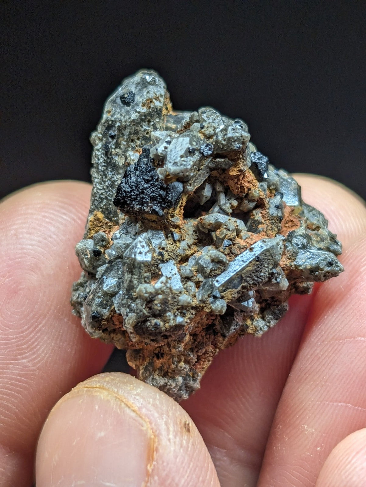 A rugged, irregularly shaped mineral specimen featuring a mix of grayish-blue crystalline formations and patches of dark black material with hints of orange rust-colored matrix.