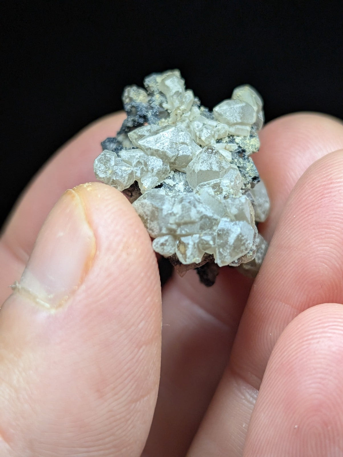 A cluster of translucent, pale greenish-white crystals with sharp facets and a rough, dark matrix base.