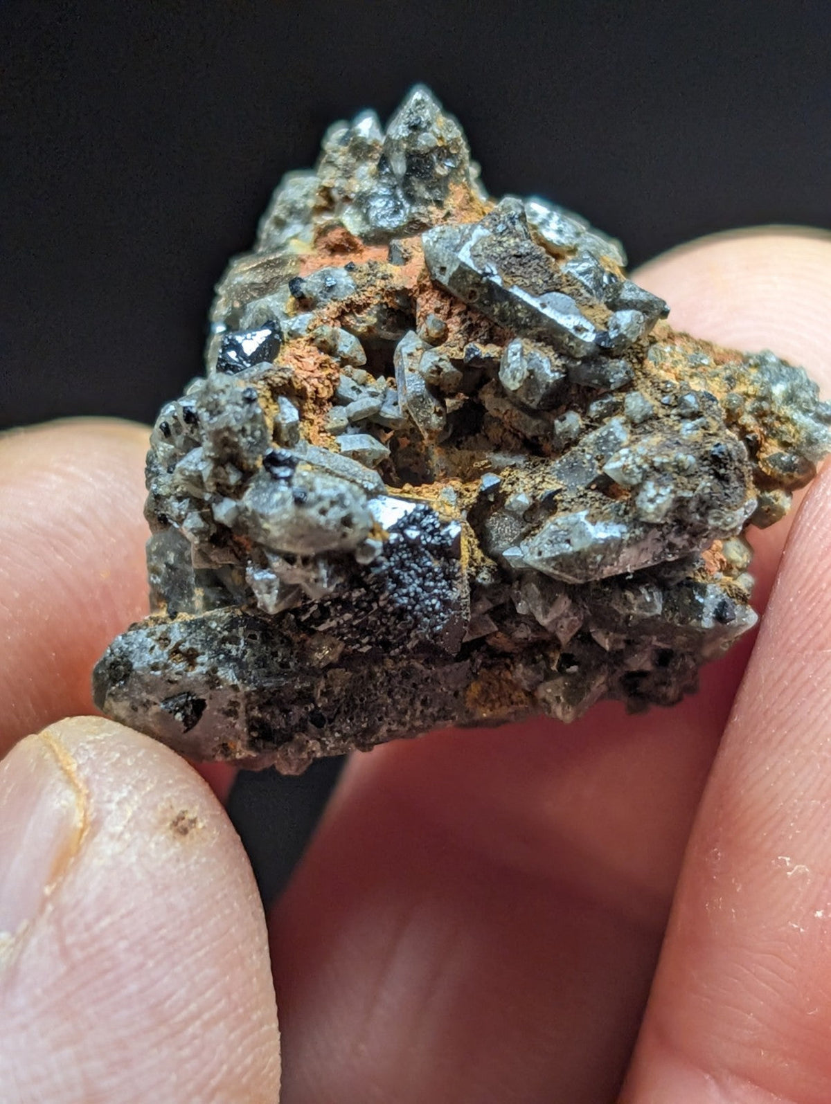 A rugged, dark gray mineral specimen with sharp crystalline formations and patches of orange rust-colored matrix.