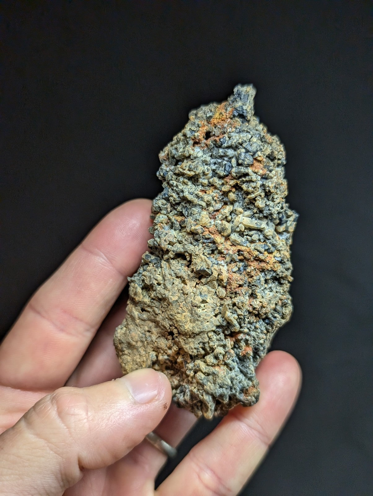 A rough, irregularly shaped mineral specimen with a mottled greenish-gray surface accented by patches of orange and brown oxidation.