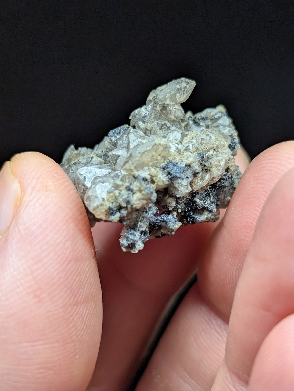 A cluster of translucent, crystalline minerals with a mix of gray and white hues, held delicately between fingers.