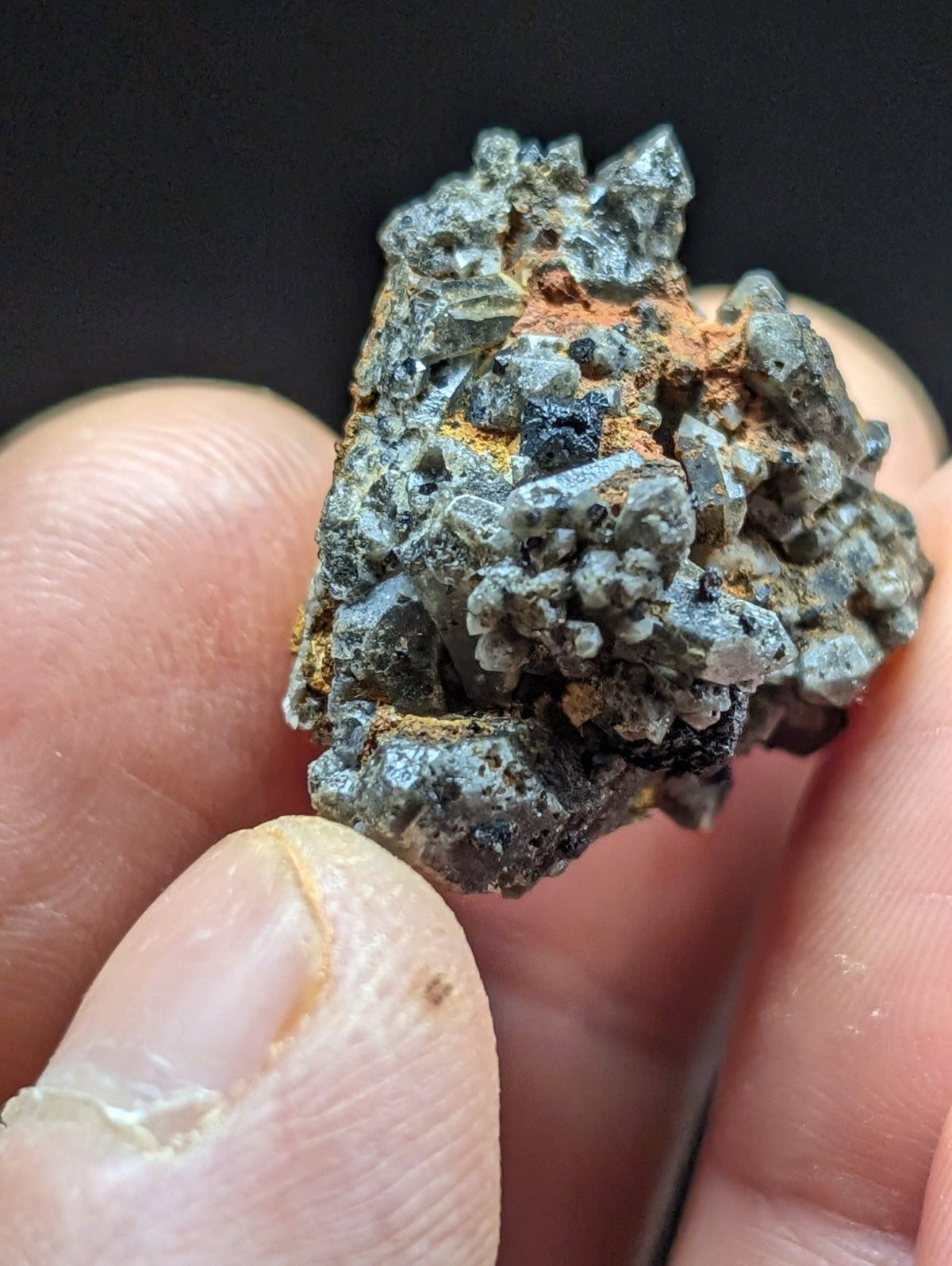 A rugged, grayish mineral specimen with crystalline formations and patches of orange rust.
