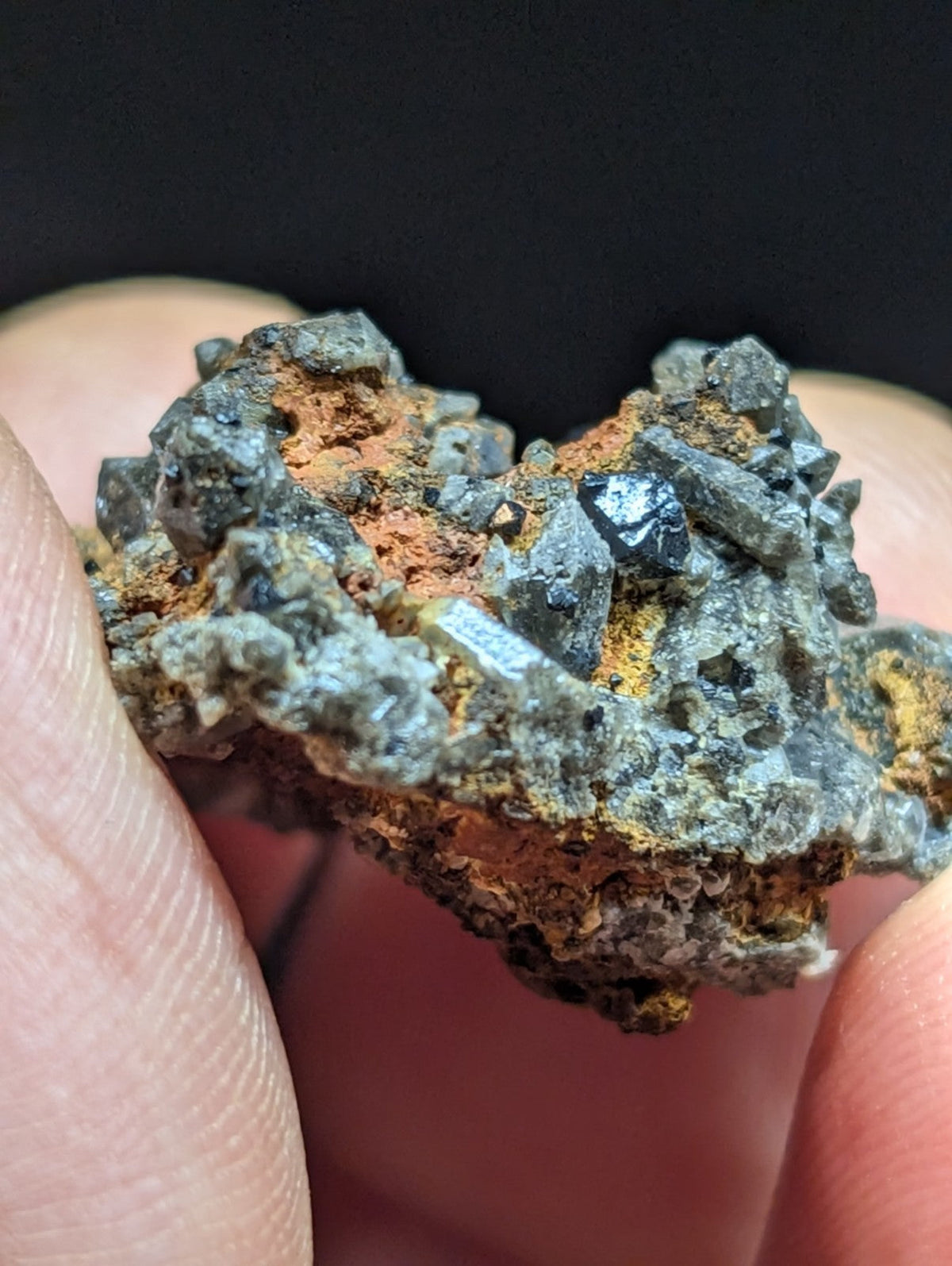 A rugged, irregularly shaped mineral specimen featuring a mix of dark gray crystalline formations and patches of orange-brown oxidation.