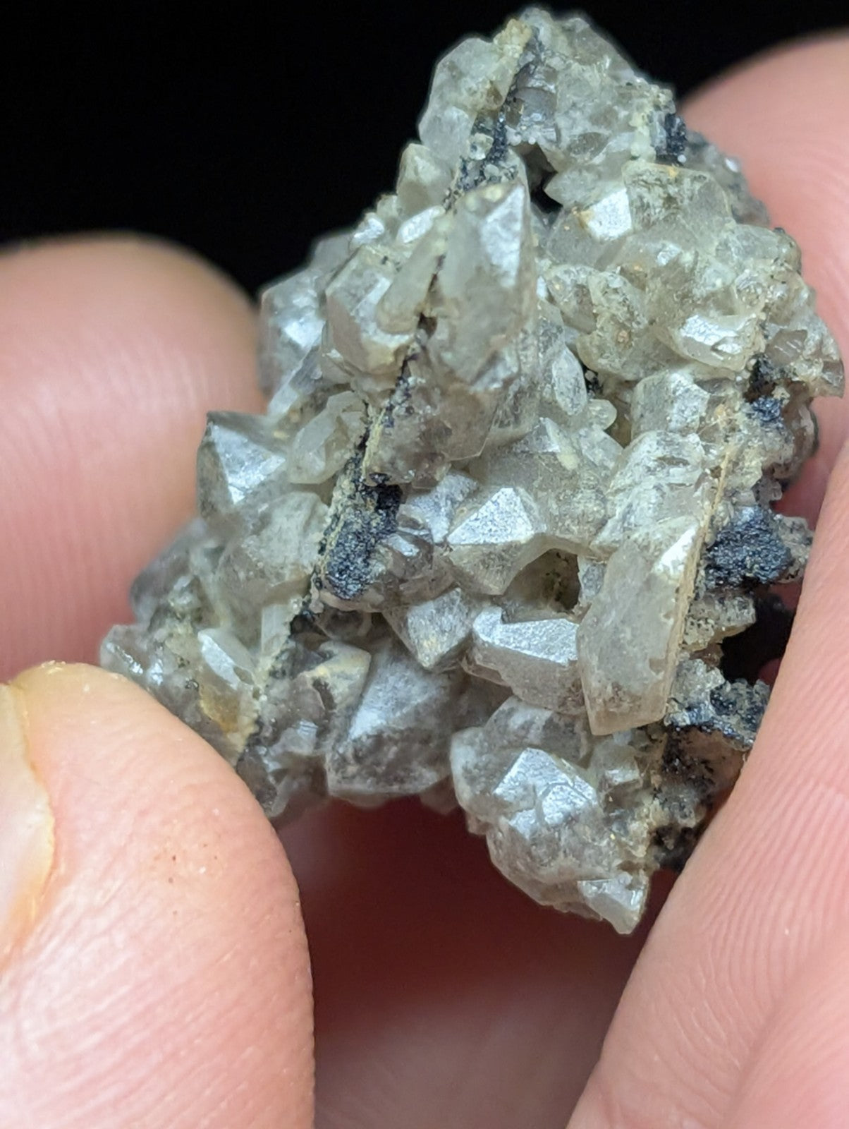 A cluster of translucent, faceted crystals with a silvery sheen and dark mineral inclusions.