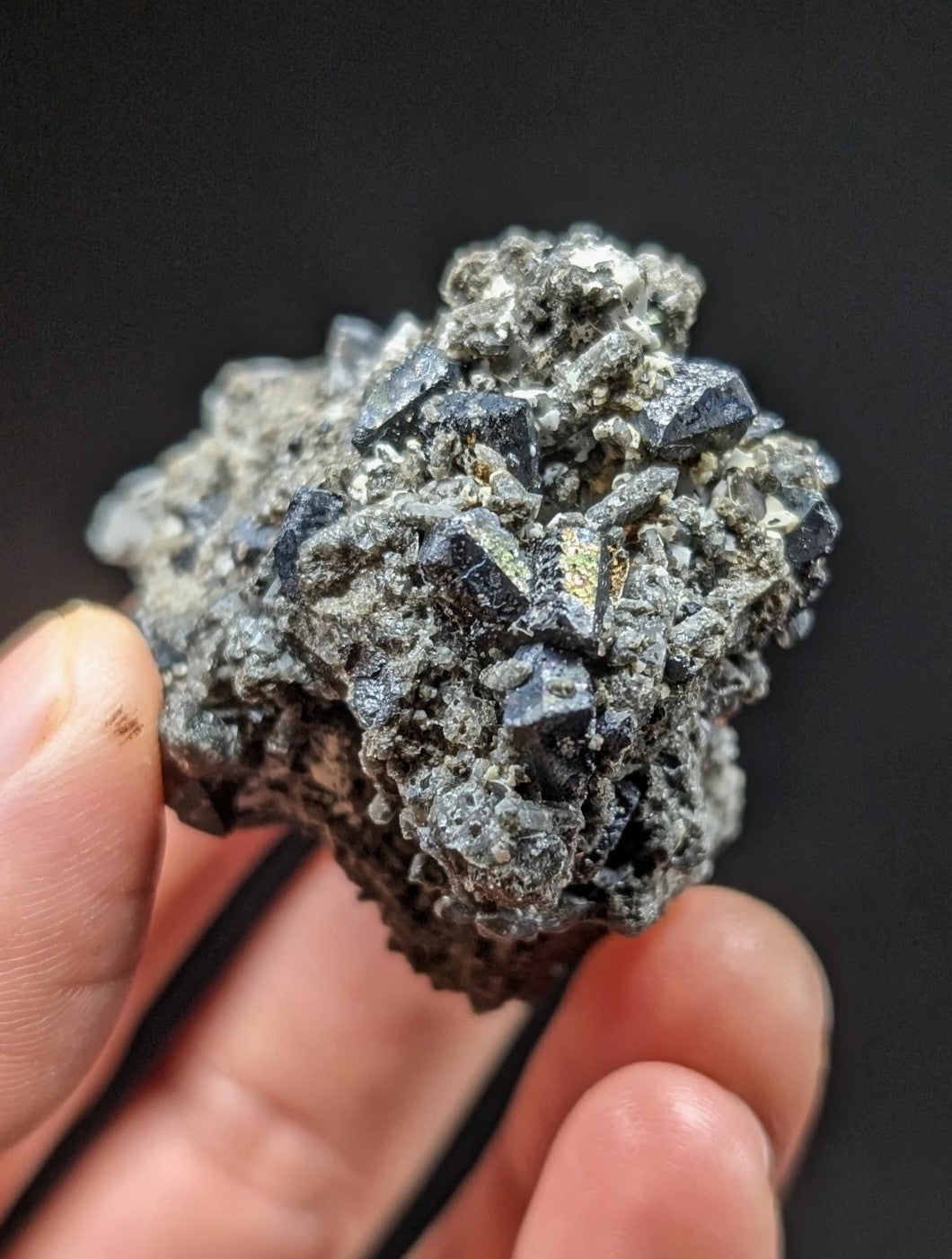 A cluster of dark, metallic pyrite crystals embedded in a rough, gray matrix.