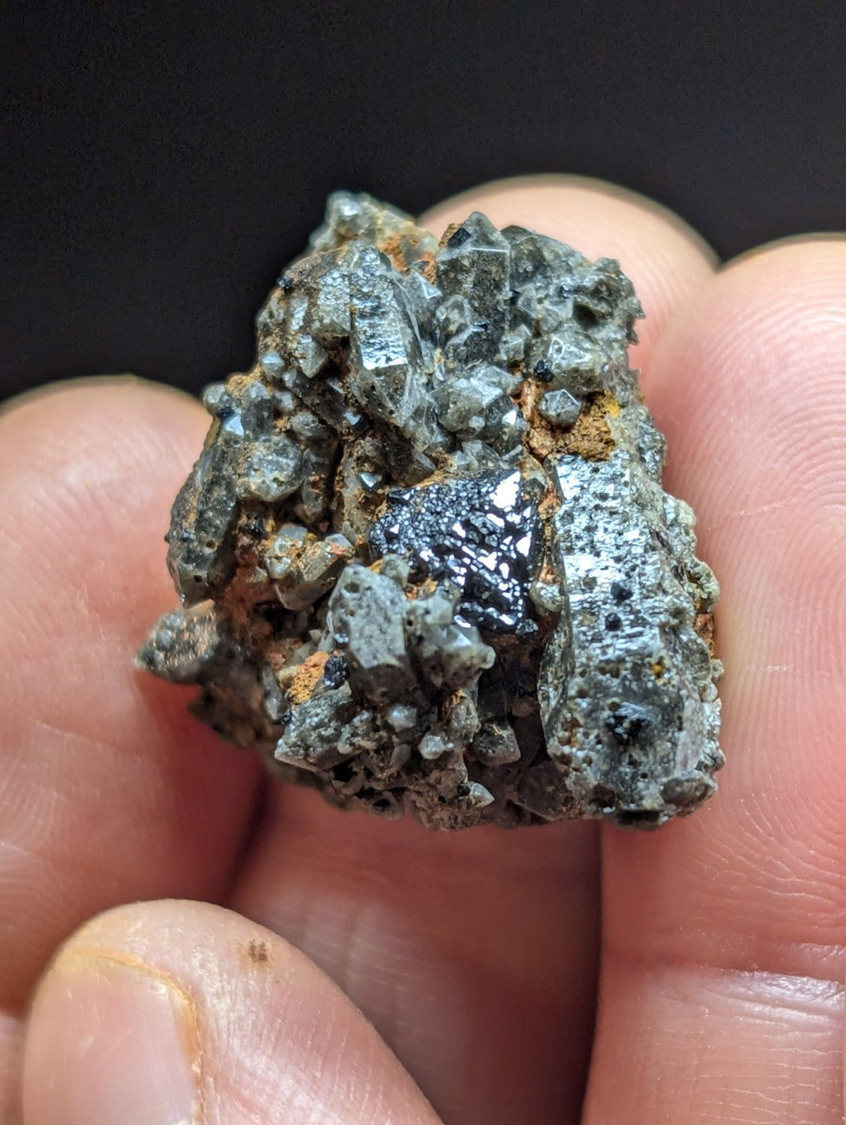A hand holds a rough, grayish mineral specimen with crystalline formations and patches of dark metallic luster.