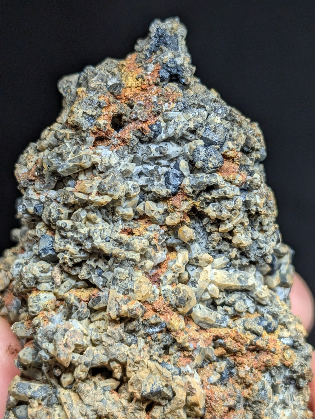 A rugged, textured mineral specimen with a mix of grayish-green crystals and patches of orange-brown oxidation.